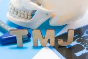 A model of a human jaw with the letters "TMJ" next to it
