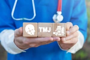 Dentist holds wooden blocks bearing the letters "TMJ"
