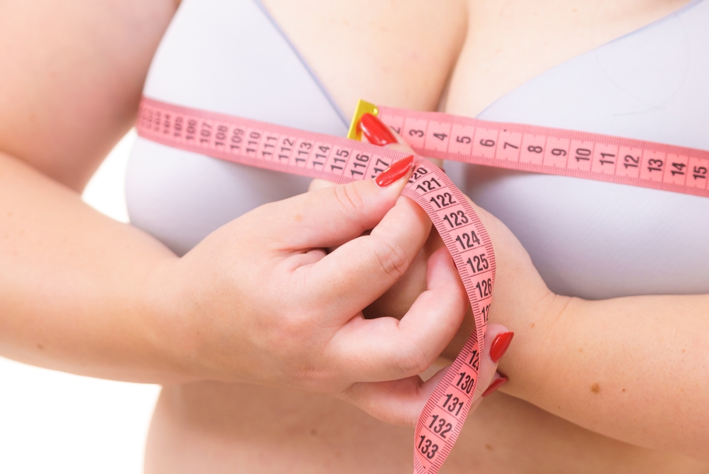 Woman measures her breasts using a tape measure before her breast reduction surgery