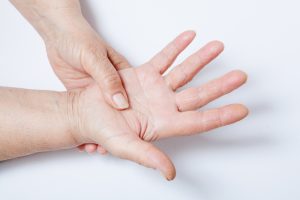 Elderly woman experience spasticity pain, pressing on her open hand