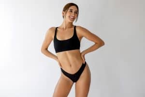 Smiling woman in black athletic wear standing with her hands on her hips, illustrating body contouring after weight loss.